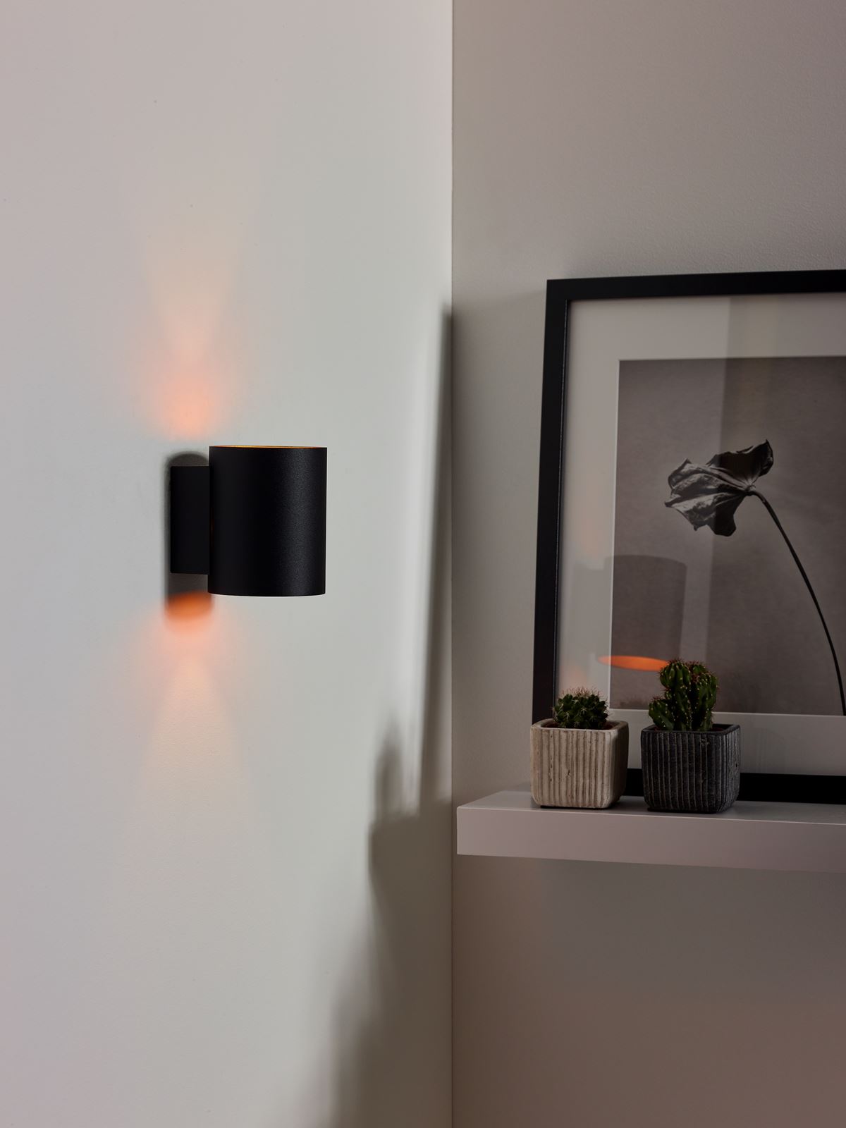 Applique Lucide Xera noire allumée sur un mur blanc de couloir