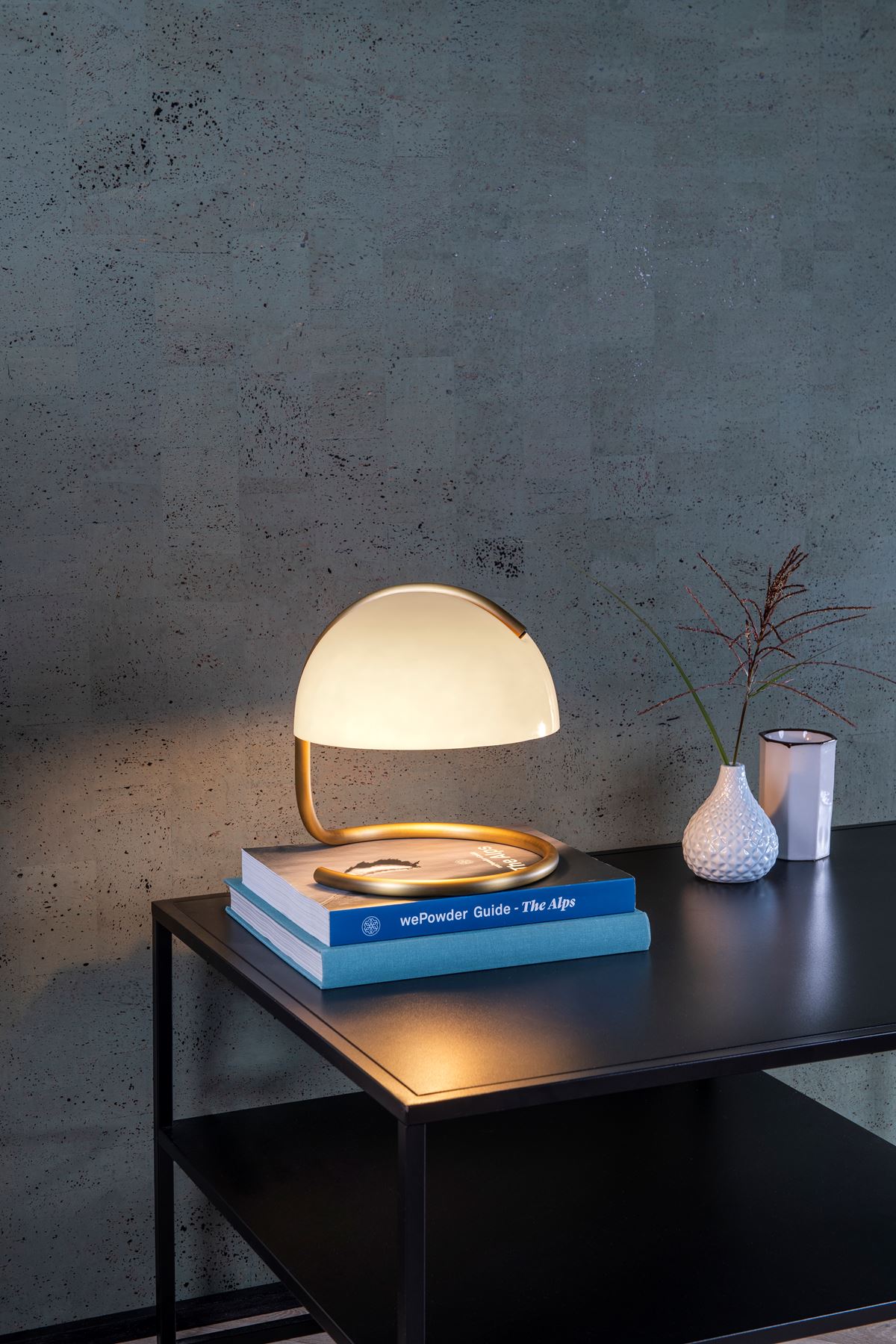Lampe Lucide Cato blanche allumée sur une table de chevet sombre