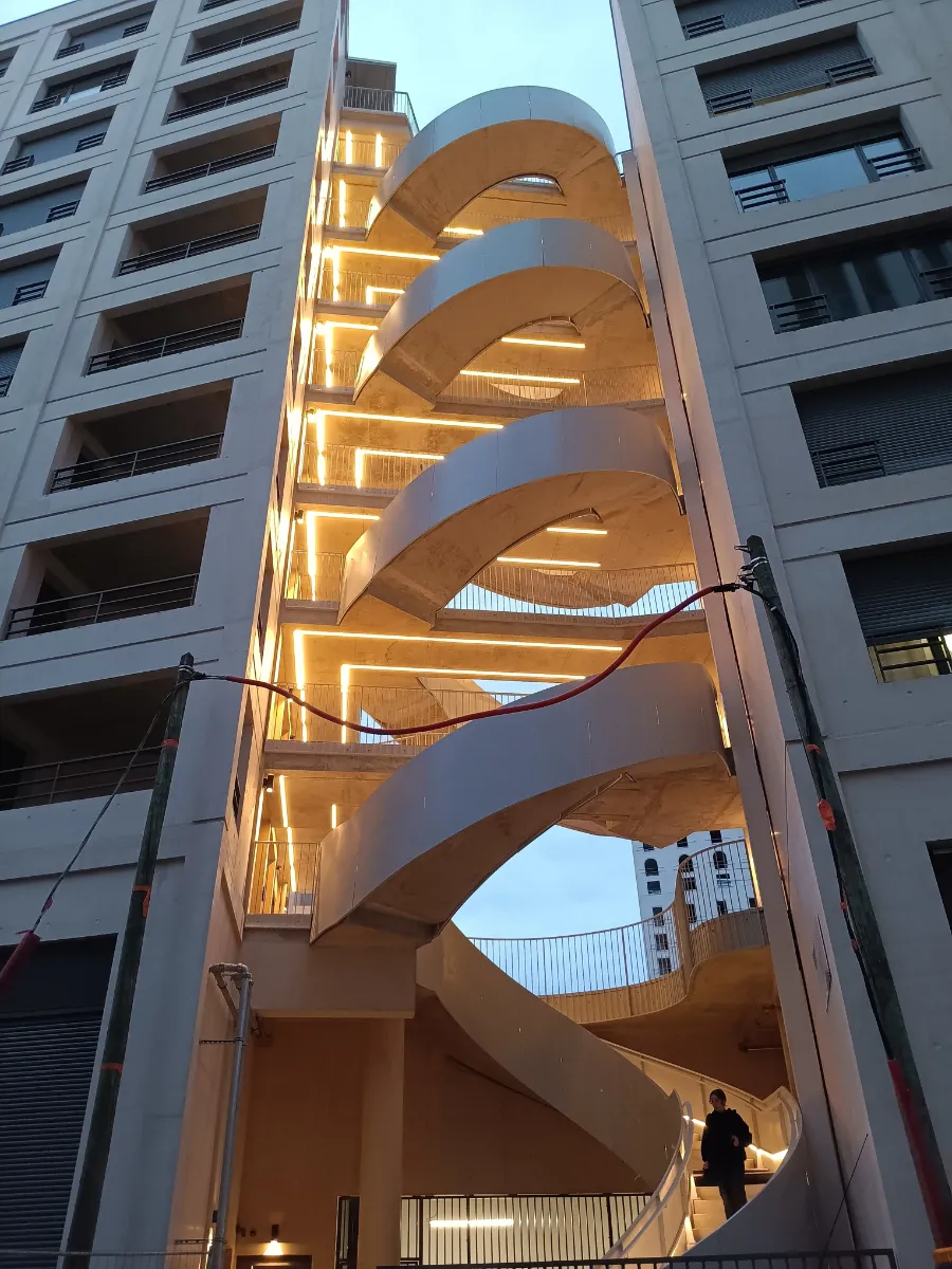 Escalier extérieur hélicoïdal en béton éclairé par des lignes de ruban LED sous les paliers et le long des coursives