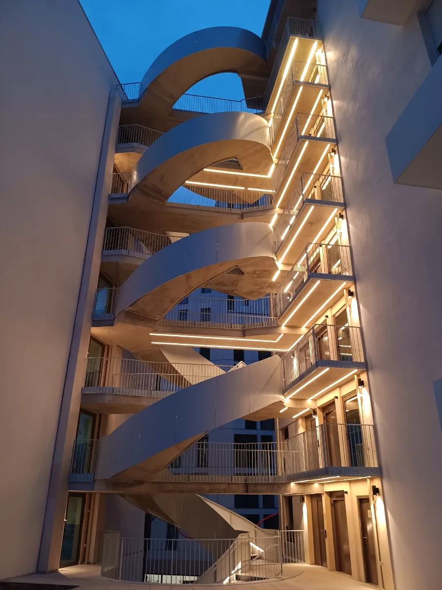 Coursives et escalier extérieur éclairés à la tombée de la nuit par des lignes continues de ruban LED en blanc chaud