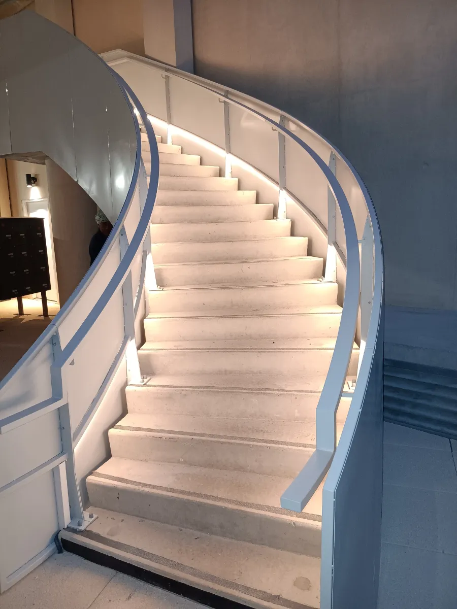 Escalier courbe éclairé par un ruban LED intégré en pied de garde-corps, qui éclaire les marches sans éblouir