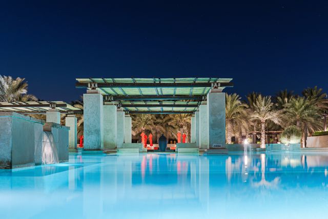 Piscine d'hôtel éclairée le soir en lumière chaude, ambiance terrasse nocturne