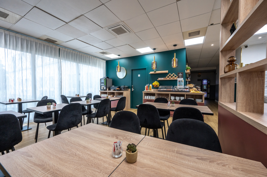 Salle petit-déjeuner de la résidence Nemea Appart'Hotel Toulouse Aéroport, suspensions en verre fumé devant un mur vert